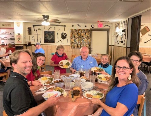A family gathers around a table, smiling and enjoying a meal together in a cozy restaurant setting.