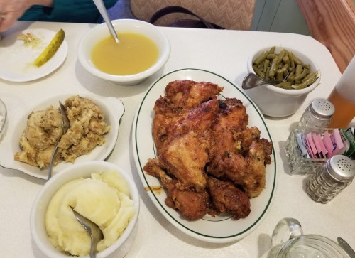 A table spread with fried chicken, mashed potatoes, stuffing, green beans, and a bowl of soup.