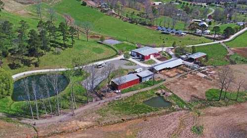 Aerial view of a rural farm with red barns, ponds, and green fields, surrounded by trees and a winding road.