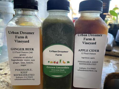 Three bottles of beverages from Urban Dreamer Farm & Vineyard: Ginger Beer, Green Smoothie, and Apple Cider, all labeled.
