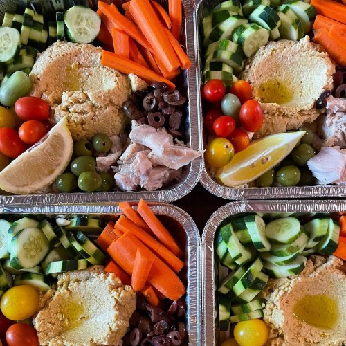 Four trays of colorful vegetable platters featuring hummus, olives, cherry tomatoes, cucumbers, and carrots.