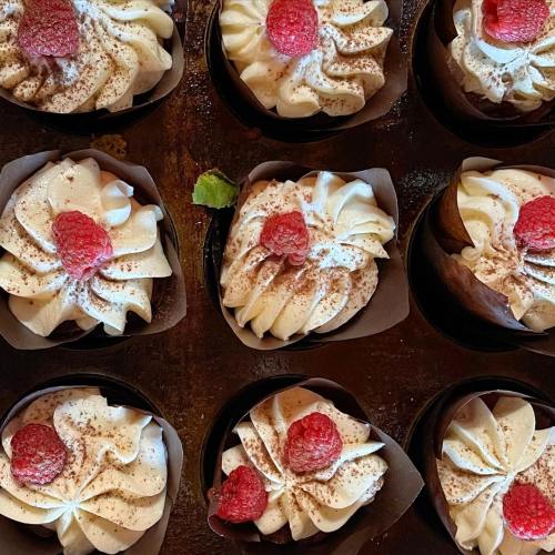 A close-up of beautifully decorated cupcakes topped with swirls of cream and fresh raspberries.