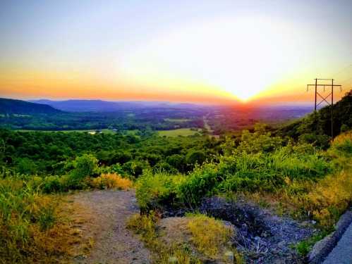 A vibrant sunset over a lush green valley, with distant mountains and a power line in the foreground.