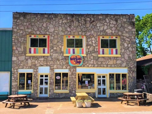 A colorful stone building with bright window frames and picnic tables outside, featuring a sign for a local business.