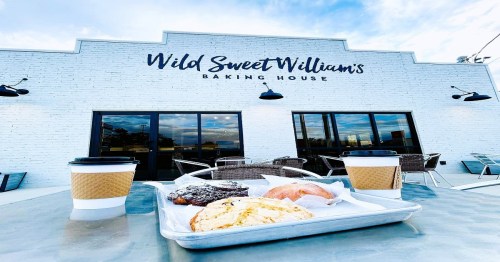 Exterior of Wild Sweet William's Baking House with coffee cups and a tray of pastries on a table in the foreground.