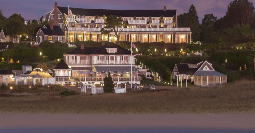 A coastal resort at dusk, featuring multiple buildings with lights and lush greenery surrounding the area.