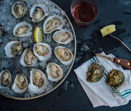 A platter of fresh oysters on ice, accompanied by a glass of rosé and lemon wedges on a cloth.