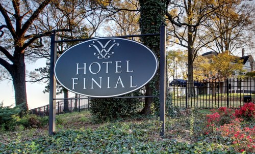Sign for Hotel Finial surrounded by trees and colorful foliage, with a building visible in the background.