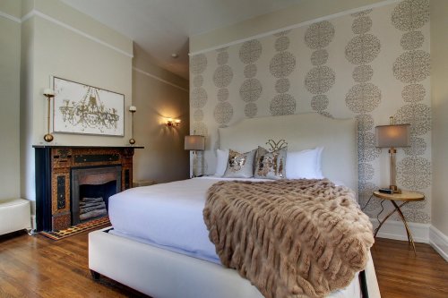 Elegant bedroom featuring a plush bed, decorative wall, fireplace, and stylish lighting. Cozy and inviting atmosphere.