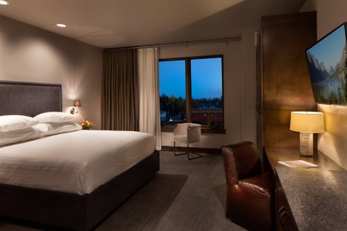 Cozy hotel room with a king bed, desk, chair, and a window showing a twilight view outside.