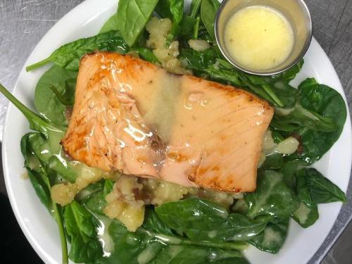 Grilled salmon fillet on a bed of fresh spinach, served with a small cup of lemon butter sauce.