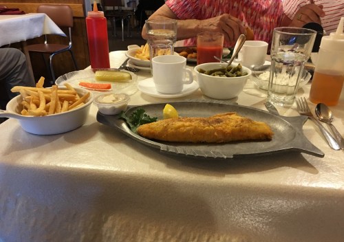 A table set with a plate of fried fish, fries, green beans, and condiments, alongside glasses of water.