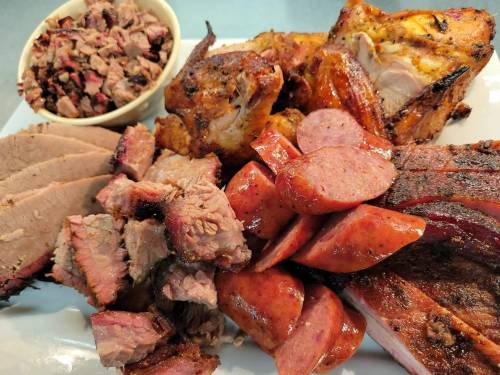 A platter of assorted meats including brisket, sausage, and grilled chicken, served with a side of chopped meat.