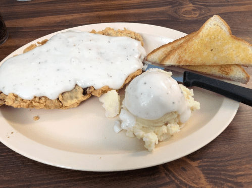 A plate with fried chicken smothered in gravy, mashed potatoes with gravy, a scoop of ice cream, and toast.