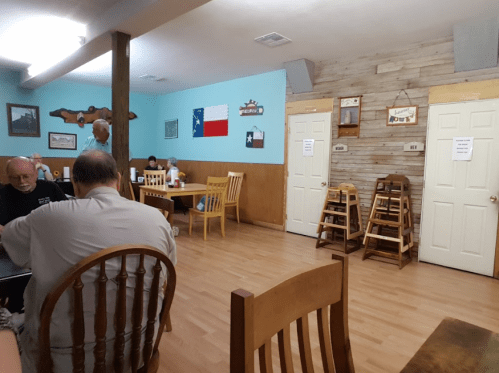 A casual dining room with wooden tables and chairs, featuring Texas-themed decor and a few patrons.