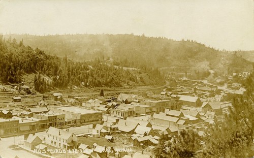A historic black-and-white photo of a small town in Idaho, surrounded by hills and dense trees.
