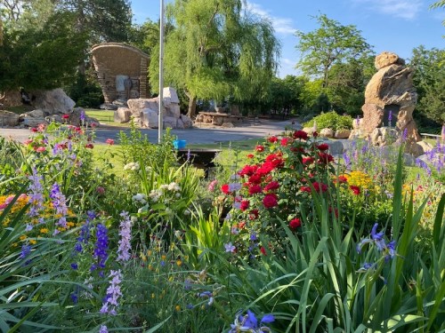 A vibrant garden filled with colorful flowers, rocks, and greenery under a clear blue sky.