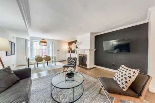 Cozy living room with a glass coffee table, modern furniture, and a dining area in the background. Stylish decor and lighting.