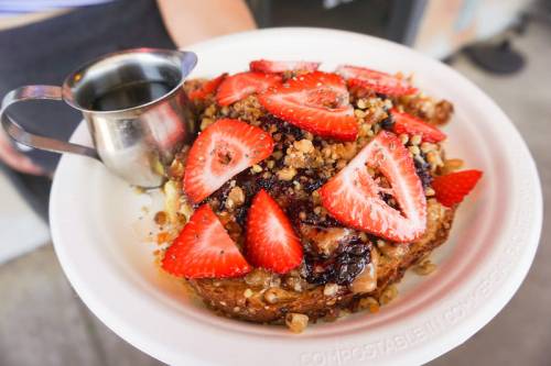 A plate of French toast topped with strawberries, granola, and a small pitcher of syrup.
