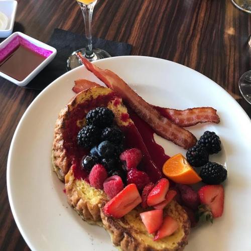 A plate of French toast topped with mixed berries, bacon strips, and a drizzle of berry sauce.