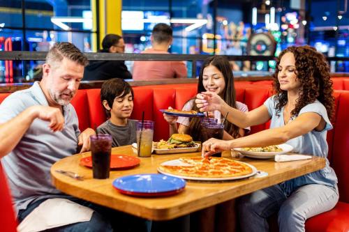 A family enjoys a meal at a restaurant, sharing pizza, burgers, and drinks at a lively table.