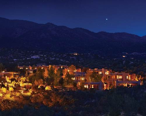 A serene night view of a hillside resort, illuminated by warm lights against a backdrop of mountains and starry sky.