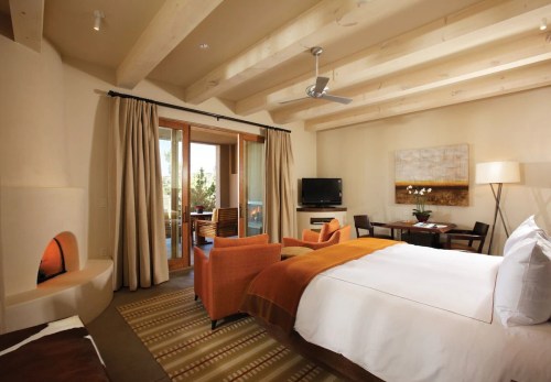Cozy hotel room with a king bed, orange chairs, a fireplace, and a balcony view. Warm, inviting decor.