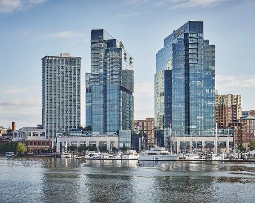 Modern glass skyscrapers reflect in the water, with boats docked in the foreground and a city skyline in the background.