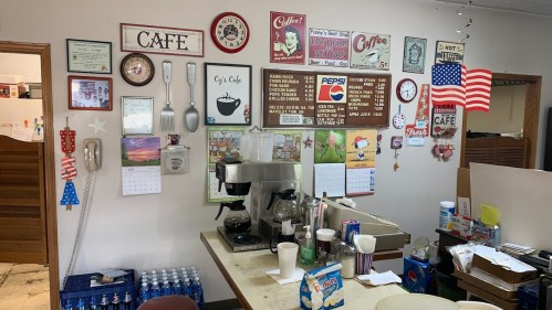 A cozy café interior featuring a wall of vintage signs, calendars, and a coffee machine on the counter.