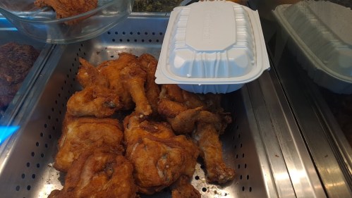 A tray of golden-brown fried chicken pieces with a takeout container on top.