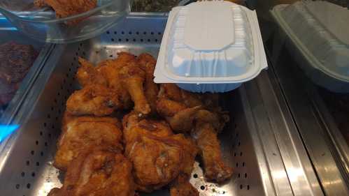 A tray of golden-brown fried chicken pieces with a takeout container on top.