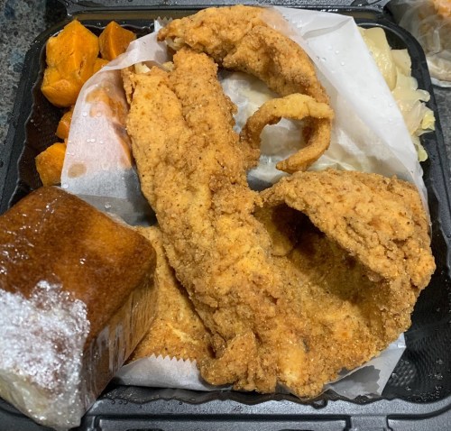 A takeout container with fried fish, sweet potatoes, and a piece of cornbread.