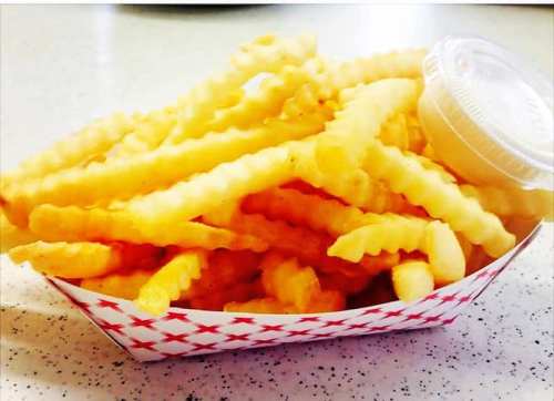 A serving of crinkle-cut fries in a red and white container, accompanied by a small cup of dipping sauce.