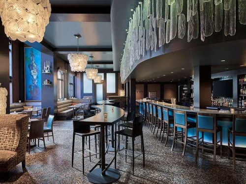 Modern bar and lounge with stylish lighting, blue accents, and a sleek design, featuring seating and a well-stocked bar.