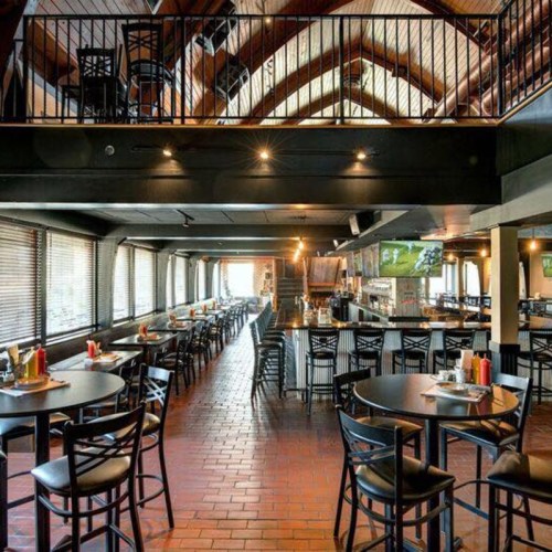 Interior of a spacious restaurant with high ceilings, wooden beams, and rows of tables and chairs.