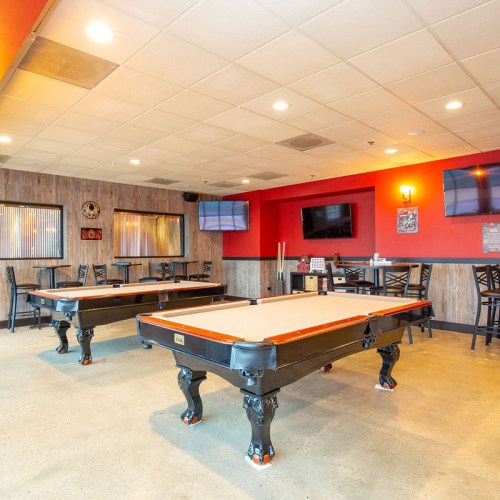 A spacious game room featuring two pool tables, red walls, and multiple TVs mounted on the walls.