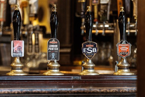Four beer taps with labels for Broadside, London Porter, ESB, and London Pride in a pub setting.