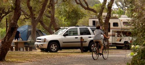A campsite with a tent, RV, and a person riding a bicycle on a path surrounded by trees.