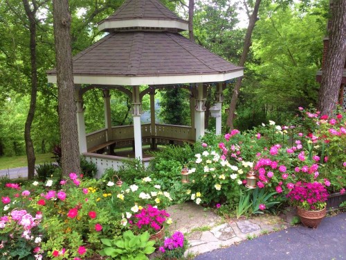 A charming gazebo surrounded by vibrant flowers and lush greenery in a serene outdoor setting.