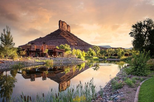 A serene landscape featuring a mountain reflected in a calm lake, surrounded by lush greenery and a sunset sky.