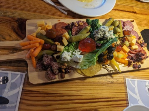 A wooden platter filled with assorted meats, cheeses, fruits, and vegetables, arranged artfully for sharing.