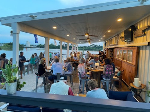 A lively outdoor gathering at a waterfront venue, with people socializing and enjoying the evening atmosphere.