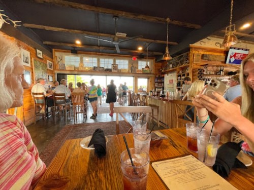 A cozy restaurant interior with patrons dining, a bar area, and two women at a table with drinks and menus.