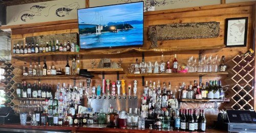 A wooden bar with various bottles of liquor, glassware, and a TV displaying a scenic view.