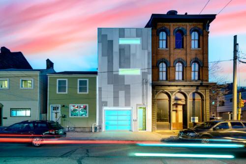 A modern building with a sleek facade stands next to a historic brick structure, under a colorful sunset sky.