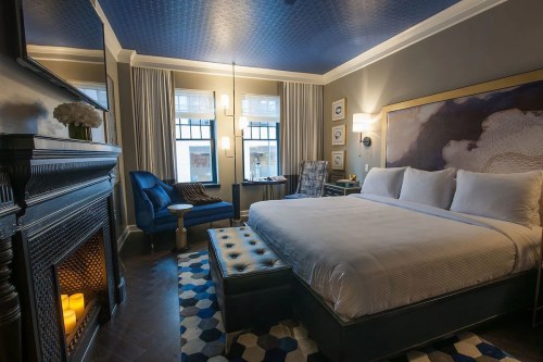 Cozy hotel room featuring a king bed, armchair, fireplace, and stylish decor with blue accents.