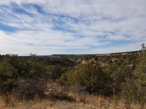 A scenic view of rolling hills and green shrubs under a partly cloudy sky.