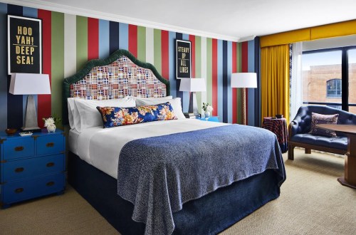 A colorful hotel room featuring a large bed, striped walls, and bright decor with a cozy seating area by the window.