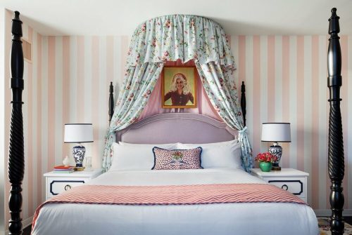 A stylish bedroom featuring a four-poster bed with floral drapery, striped walls, and elegant decor.