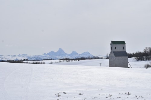 A snow-covered landscape with a solitary building and distant mountains under a cloudy sky.